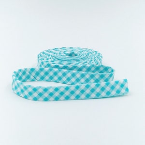 May include: A roll of turquoise and white gingham ribbon. The ribbon is folded in half and the ends are curled.