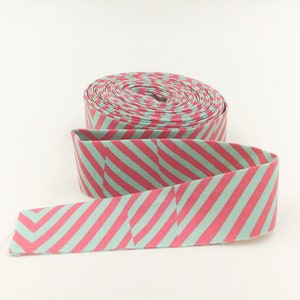 May include: A roll of pink and light blue striped fabric ribbon. The ribbon is rolled up and the end is unfurled, showing the pattern.