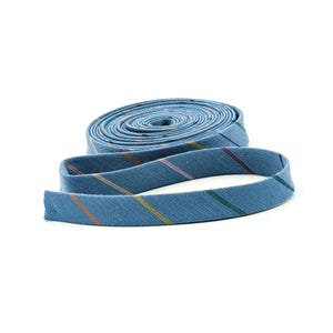 May include: A coil of blue bias tape featuring a woven twill texture and thin, diagonal stripes in shades of orange, yellow, pink, and dark green. The fabric strip is wound into a flat, circular roll with one end extending outward from the center.