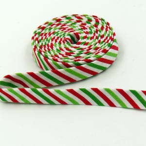 May include: A coiled roll of fabric bias tape featuring a repeating diagonal stripe pattern in vibrant red, bright green, and white. The textile strip is wound into a tight circular spool with one end extending outward across the surface.
