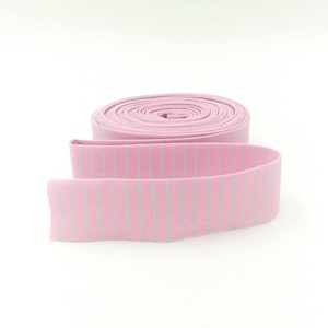 May include: A roll of pink and white striped elastic trim. The trim is rolled up and the end is unfurled, showing the striped pattern.