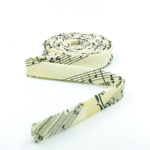 May include: A roll of off-white fabric ribbon with a black musical note print. The ribbon is rolled up and the end is unfurled, showing the pattern.
