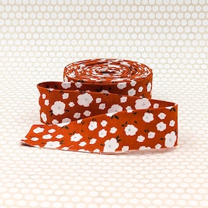 May include: A roll of floral fabric with a burnt orange background and white flower pattern. The fabric is unrolled, revealing the pattern and texture. The fabric is likely used for sewing, quilting, or other crafts.