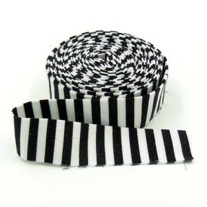 May include: A roll of fabric ribbon featuring a repeating pattern of vertical black and white stripes. The ribbon is coiled into a circular shape with one end extending outward, displaying the consistent high-contrast striped design throughout.