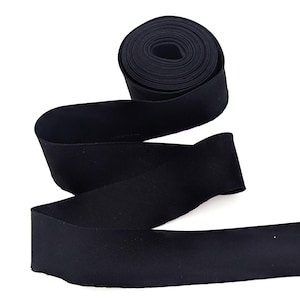 May include: A roll of black elastic ribbon, unspooled and lying flat. The ribbon is a solid, matte black color. The ribbon is likely used for sewing, crafting, or other DIY projects.