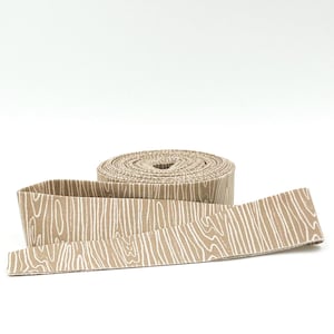 May include: A roll of brown fabric with a white woodgrain pattern. The fabric is rolled up and a section is unrolled to show the pattern.