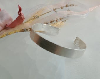 May include: A silver bangle bracelet with a hammered finish. The bracelet is open and has a smooth, polished surface.