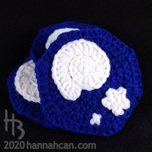 May include: A set of three crocheted blue and white coasters featuring a seashell and star design. The coasters are made with a soft, textured yarn.