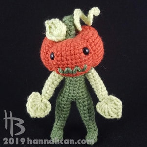 May include: A crocheted pumpkin character with a green body, orange head, and green stem. The pumpkin has a friendly face with black eyes and a green mouth.