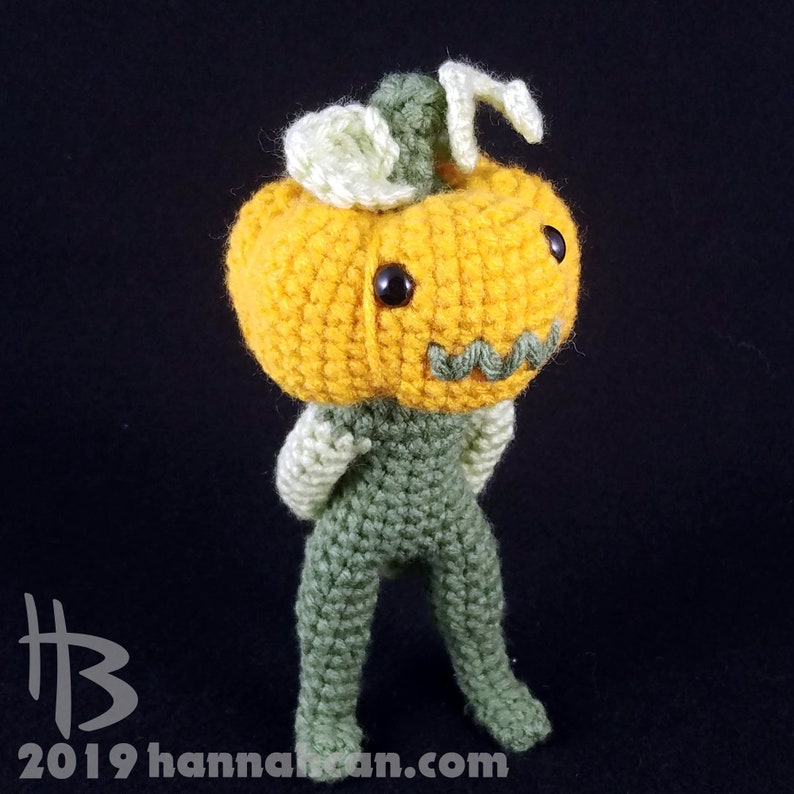 May include: A crocheted pumpkin character with a green body and a yellow pumpkin head. The pumpkin has a green stem and a friendly face with black eyes.