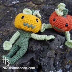 May include: Two crocheted pumpkin characters, one orange and one yellow, with green stems and leaves. The orange pumpkin is sitting on a rock, while the yellow pumpkin is standing on the rock with its arms outstretched.