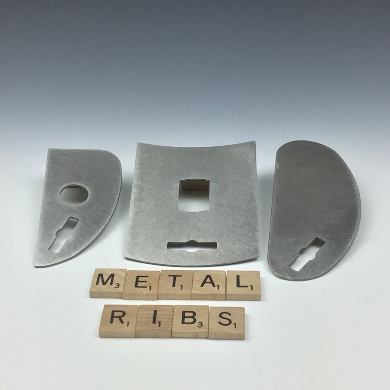 May include: Three metal pieces with cutouts in the shape of a keyhole, a rectangle, and a circle. The pieces are arranged on a white surface with the word "METAL" spelled out in Scrabble tiles below them. The word "RIBS" is spelled out in Scrabble tiles below the word "METAL".
