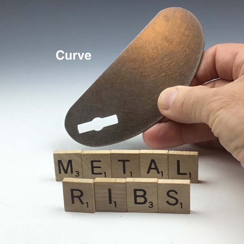 May include: A metal rib tool with a curved shape and a hole in the center. The tool is labeled "Curve" and is sitting on top of wooden letter tiles that spell out "METAL RIBS".