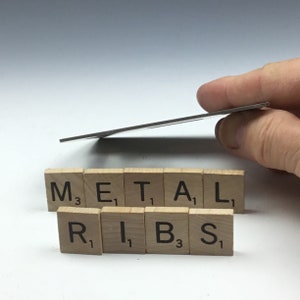 May include: A close-up of wooden letter tiles spelling out the words "METAL RIBS". The tiles are arranged in two rows, with the first row spelling out "METAL" and the second row spelling out "RIBS". Each tile has a letter and a number on it, indicating the point value of the letter in a game of Scrabble.