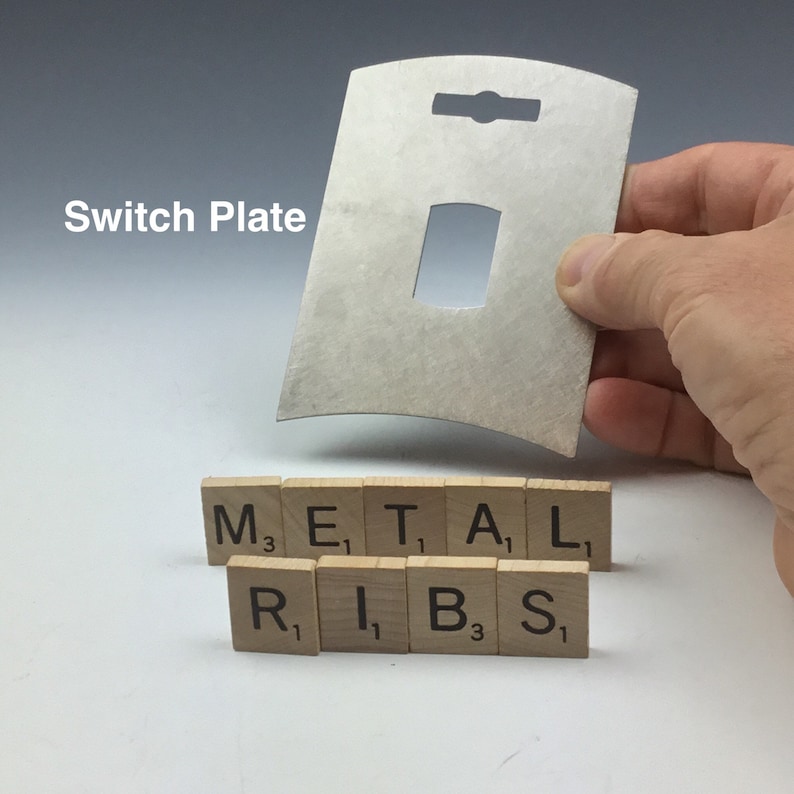 May include: A silver metal switch plate with a cutout for a light switch. The plate is curved and has a hole for hanging. The words "Switch Plate" are written in black text on a white background. The words "METAL RIBS" are spelled out using letter tiles.