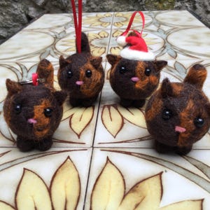 Pode incluir: Quatro enfeites de gato de feltro marrom e laranja com olhos pretos. Um gato está usando um chapéu de Papai Noel vermelho.