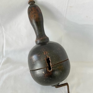May include: A dark brown wooden bell with a handle and a metal lever. The bell is split in half and has a hole in the side.