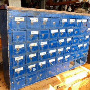 May include: A vintage blue wooden cabinet with 48 drawers, each with a small label. The cabinet is distressed and has a rustic look.