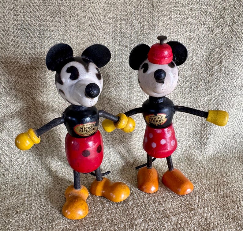 Puede incluir: Dos figuras de madera vintage de Mickey y Minnie Mouse. Mickey tiene cabeza y orejas negras, cara blanca, pantalones cortos rojos y guantes y zapatos amarillos. Minnie lleva una falda roja con lunares blancos y un sombrero rojo.