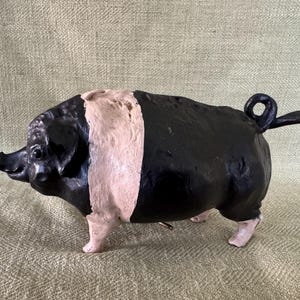 May include: A black and pink cast iron pig figurine. The pig has a curled tail and stands on four legs.