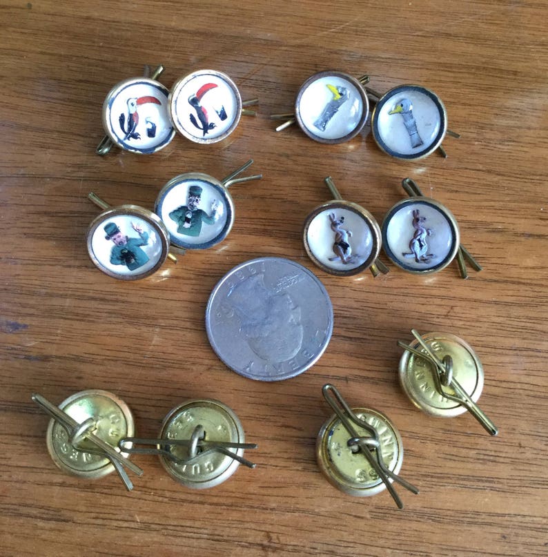 May include: A collection of 12 vintage buttons with various images, including a toucan, a kangaroo, a man in a top hat, and a man in a green suit. The buttons are gold-toned and have a glass-like finish. A US quarter is included for size reference.