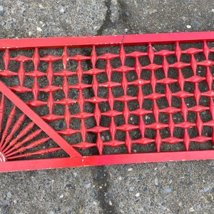 May include: A red wooden lattice panel with a diamond pattern. The panel has a triangular section with a sunburst design.
