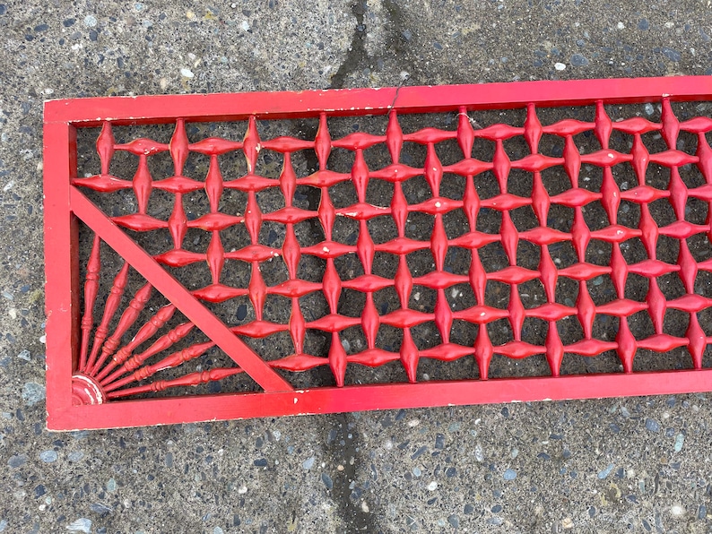 May include: A red wooden lattice panel with a diamond pattern. The panel has a triangular section with a sunburst design.