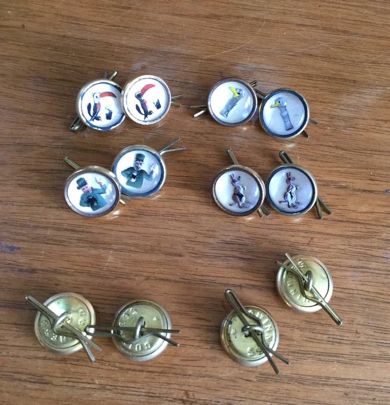 May include: A collection of ten vintage gold-toned buttons with various images, including a toucan, a bird, a man in a top hat, a rabbit, and a plain button.