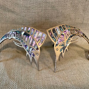 May include: Two silver marlin fish sculptures with iridescent mother-of-pearl inlay. The marlin are leaping out of the water with their tails up.