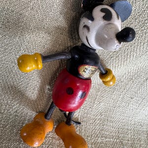 Puede incluir: Juguete de madera vintage de Mickey Mouse con orejas negras, cara blanca y nariz negra. La figura tiene un torso negro, pantalones cortos rojos y guantes y zapatos amarillos. Las palabras "Mickey Mouse" son visibles en el pecho.
