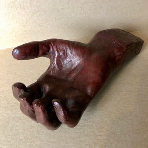 May include: A dark brown hand sculpture with an open palm, made of a textured material. The hand is slightly angled and appears to be reaching out.
