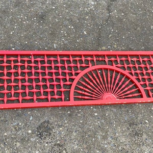 May include: A red wooden lattice panel with a decorative sunburst design. The panel is made of thin strips of wood that are woven together to create a geometric pattern.