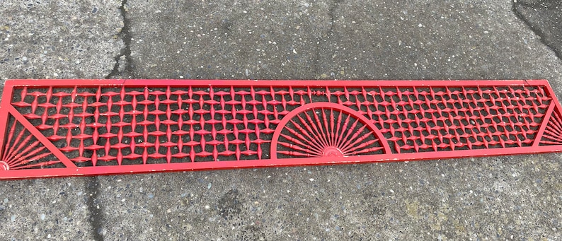 May include: A red wooden lattice panel with a decorative sunburst design. The panel is made of thin strips of wood that are woven together to create a geometric pattern.