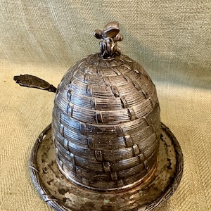 May include: Silver plated honey pot with a bee on the lid and a small spoon. The pot is shaped like a honeycomb.
