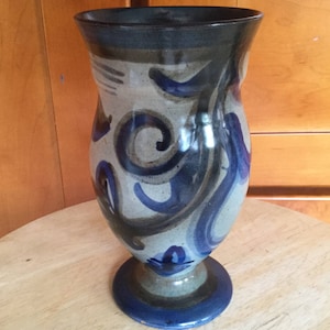 May include: A ceramic vase with a blue and brown swirl design. The vase has a wide mouth and a narrow base.