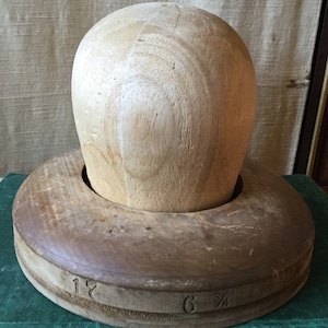 May include: A wooden hat block with a round top and a flat base. The base has markings that read "6 3/4" and "1 1/2".