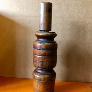 May include: A wooden, turned, and segmented bottle stopper with a hole in the top. The stopper is brown and has a natural wood finish.