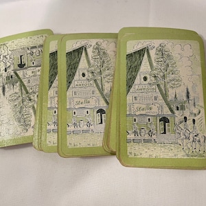 May include: A set of five vintage playing cards featuring a green and white illustration of a building with the text "Biere Artois Stella Artois" on the front. The cards are in good condition with some wear and tear.