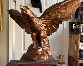 May include: A vintage, gold-painted eagle statue on a wooden music box with the text "Hohner Harmonicas Patent applied for".