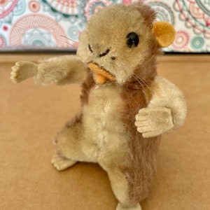 May include: A vintage plush toy of a brown and white squirrel with black eyes and a pink nose. The squirrel is standing on all fours with its arms outstretched.