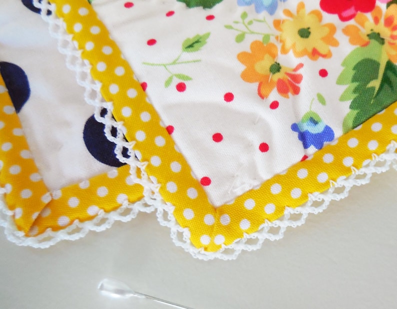 K&ouml;nnte beinhalten: Nahaufnahme eines wei&szlig;en Stoffes mit gelbem Tupfenrand und wei&szlig;er H&auml;kelkante. Der Stoff hat ein Blumenmuster mit roten, gelben und blauen Blumen.