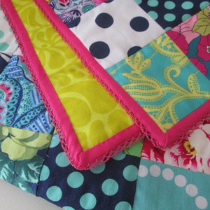 Puede incluir: Una colcha de retazos con una variedad de telas coloridas, incluyendo patrones florales, lunares y dise&ntilde;os de cachemira. La colcha est&aacute; bordeada con un ribete de crochet rosa y blanco.