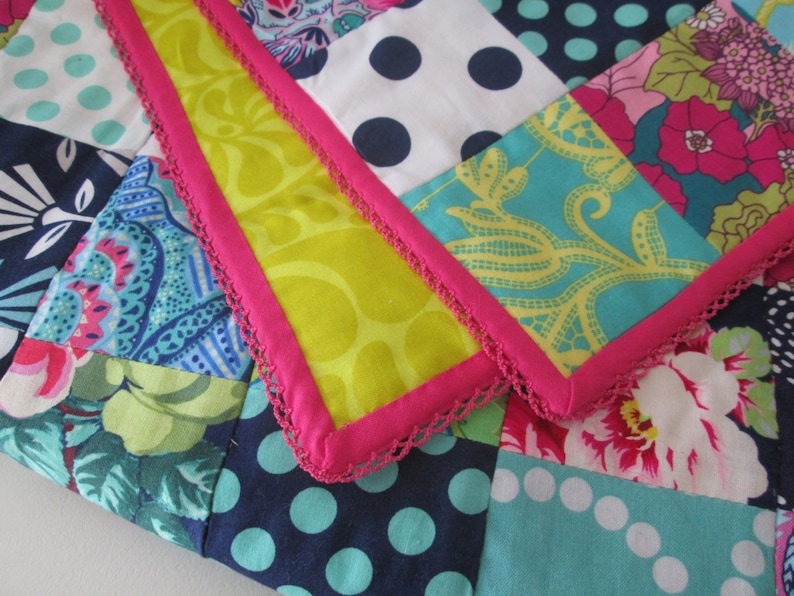 Puede incluir: Una colcha de retazos con una variedad de telas coloridas, incluyendo patrones florales, lunares y dise&ntilde;os de cachemira. La colcha est&aacute; bordeada con un ribete de crochet rosa y blanco.