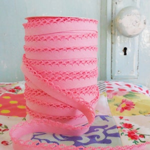 May include: A roll of pink elastic trim with a delicate lace pattern. The trim is rolled up and ready to be used for sewing or crafting projects.