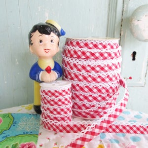 May include: Two spools of red and white gingham ribbon with white crochet trim. The ribbon is wound around the spools and is ready to be used for crafting or decorating.