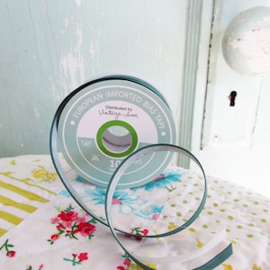 Könnte beinhalten: Eine Rolle grünes Schrägband mit der Aufschrift "European Imported Bias Tape" und "Vintage doors". Das Band liegt auf einem Patchwork-Quilt mit Blumen- und Streifenmustern. Im Hintergrund eine hellblaue Tür.