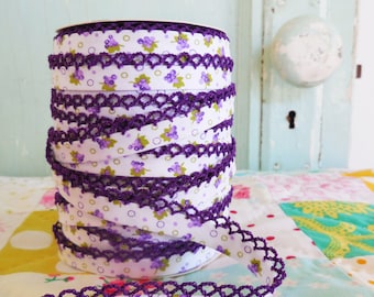 Könnte beinhalten: Eine Rolle elastischer Besatz in Lila und Weiß mit einem Blumenmuster. Der Besatz hat einen gehäkelten Rand.