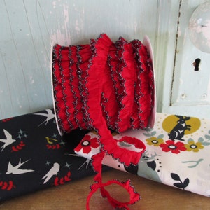 May include: A roll of red ruffled ribbon with black trim sits next to two fabric pieces. One fabric is black with white birds and red accents. The other is white with a black rabbit and floral design. Decorative craft supplies.