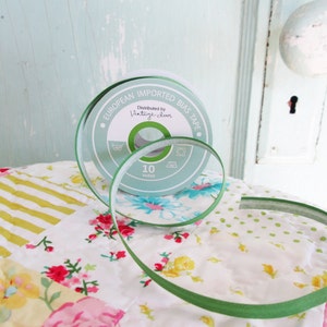 May include: A spool of green bias tape with a label that reads "European Imported Bias Tape" and "Distributed by Vintage Chic". The tape is on a white and green floral fabric.