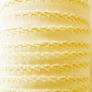 Puede incluir: Un rollo de ribete de crochet blanco marfil con un borde festoneado. El ribete est&aacute; hecho de un material suave y delicado y tiene un brillo sutil.